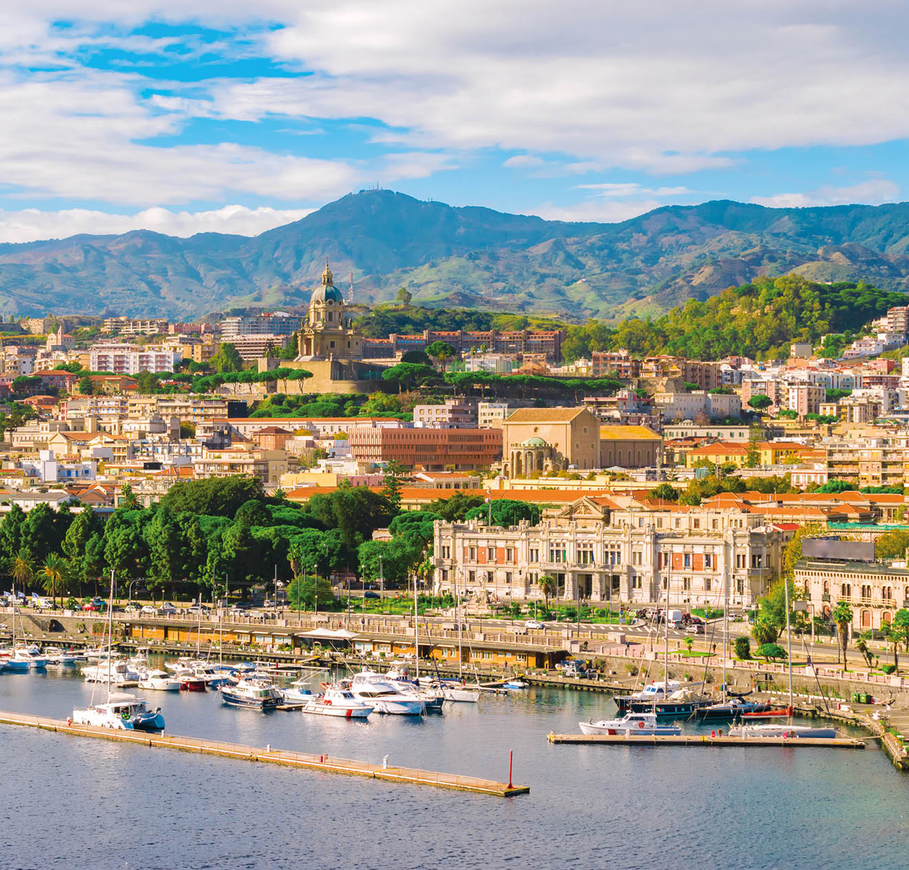 Cityscape of Messina, Sicily, Italy. Multi colored image with buildings, cathedral, mountains, blue sky with clouds, boats and yachts in the harbor or cruise port of Messina.