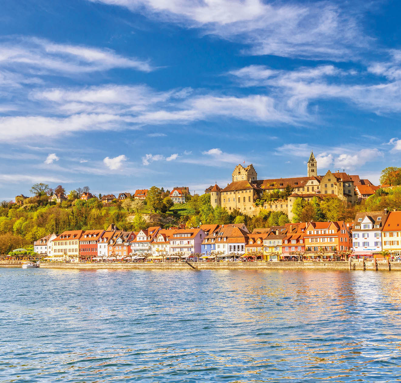 Panoramic view on the charming medieval city of Meersburg, located at the Lake Constance (Bodensee), with a sailing boat passing the city´s beautiful waterfront in the lower town and it´s landmark castles in the upper town. 