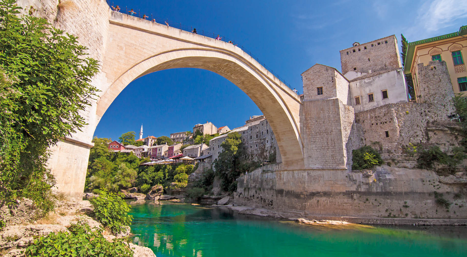 Old Bridge (Stari Most), UNESCO World Heritage, and emerald river Neretva among rocks and old city buildings in summer sun lights. Mostar, Bosnia and Herzegovina
