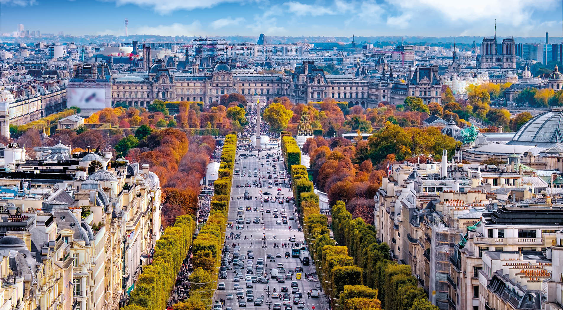The Avenue des Champs- lys es in late autumn seen from the Arc de Triomphe. Orange and yellow tree leafs with heavy traffic in the middle. Old buildings on both sides.