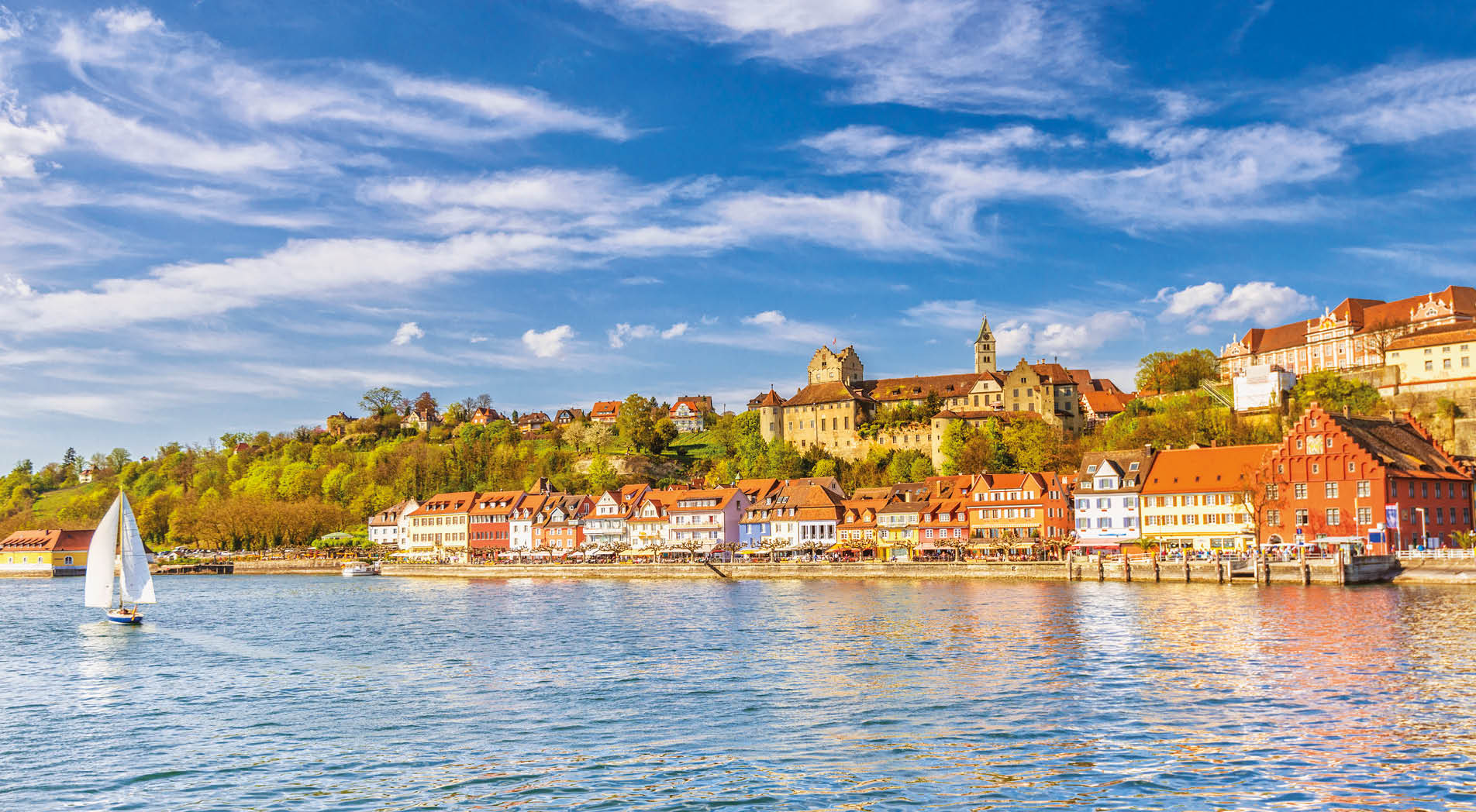 Panoramic view on the charming medieval city of Meersburg, located at the Lake Constance (Bodensee), with a sailing boat passing the city´s beautiful waterfront in the lower town and it´s landmark castles in the upper town. 