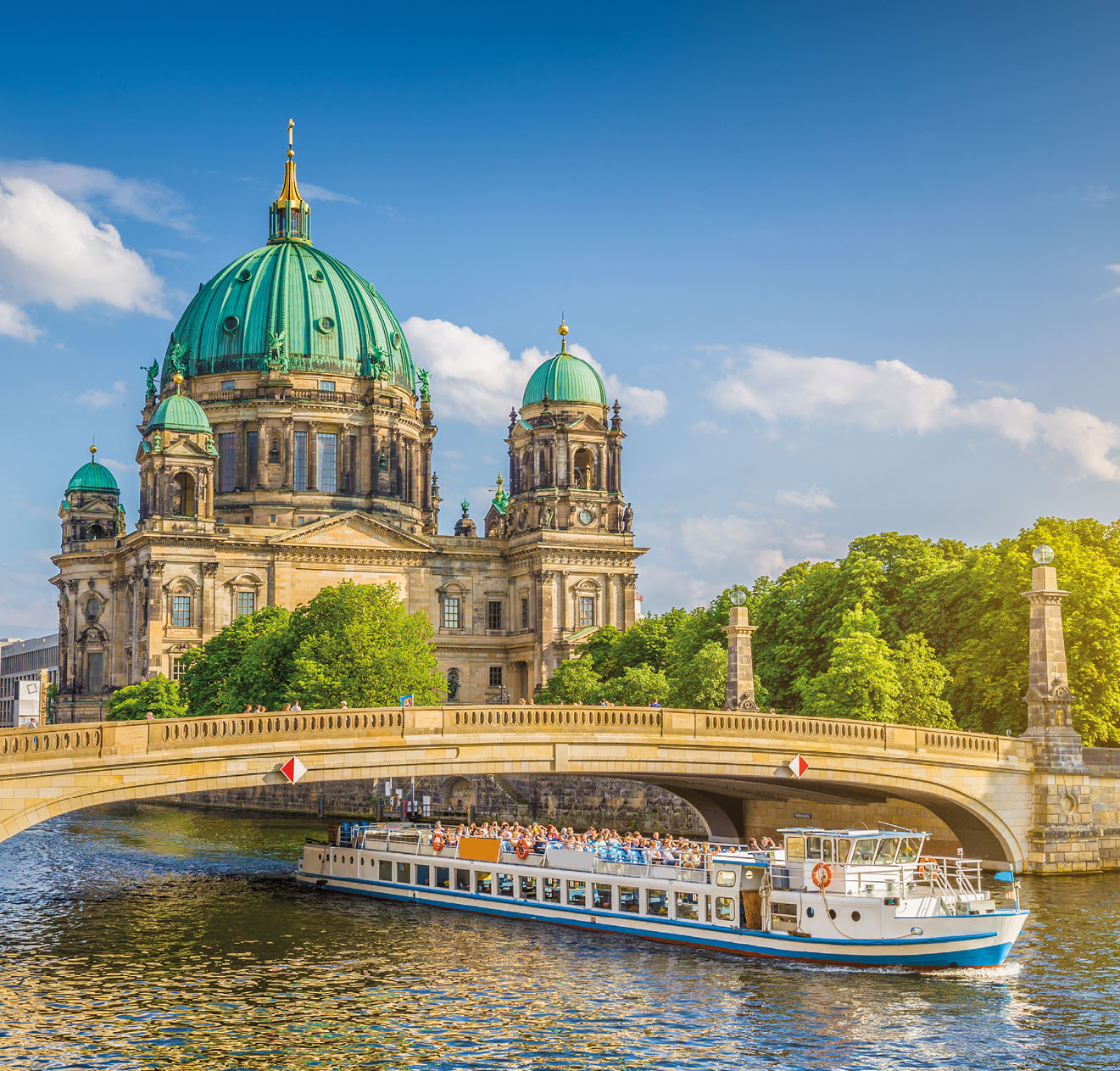 Beautiful view of historic Berlin Cathedral (Berliner Dom) at famous Museum Island with ship passing Friedrichsbrucke bridge on Spree river in golden evening light at sunset in summer, Berlin, Germany