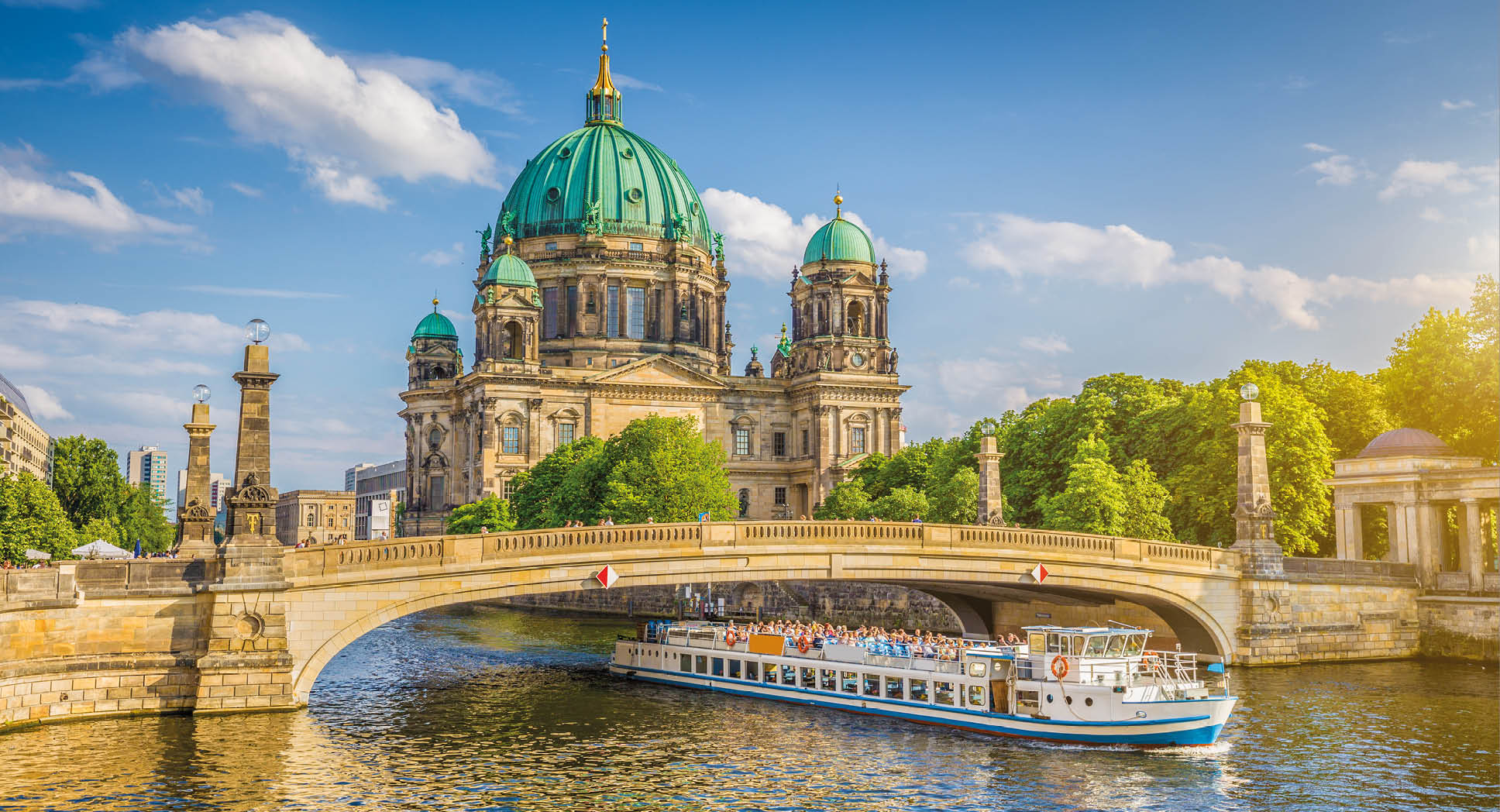 Beautiful view of historic Berlin Cathedral (Berliner Dom) at famous Museum Island with ship passing Friedrichsbrucke bridge on Spree river in golden evening light at sunset in summer, Berlin, Germany