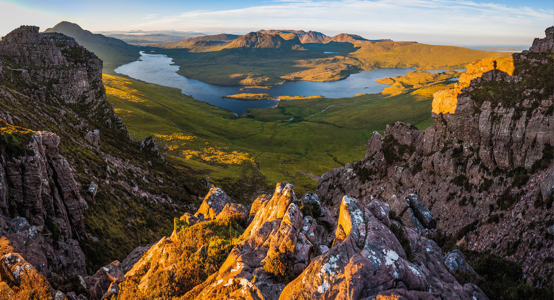 Golden sunrise illuminating the dramatic mountain peaks, glens and ridges of Coigach overlooking Loch Lugainn on the wild and remote peninsula deep in the Northwest Highlands of Scotland, UK.