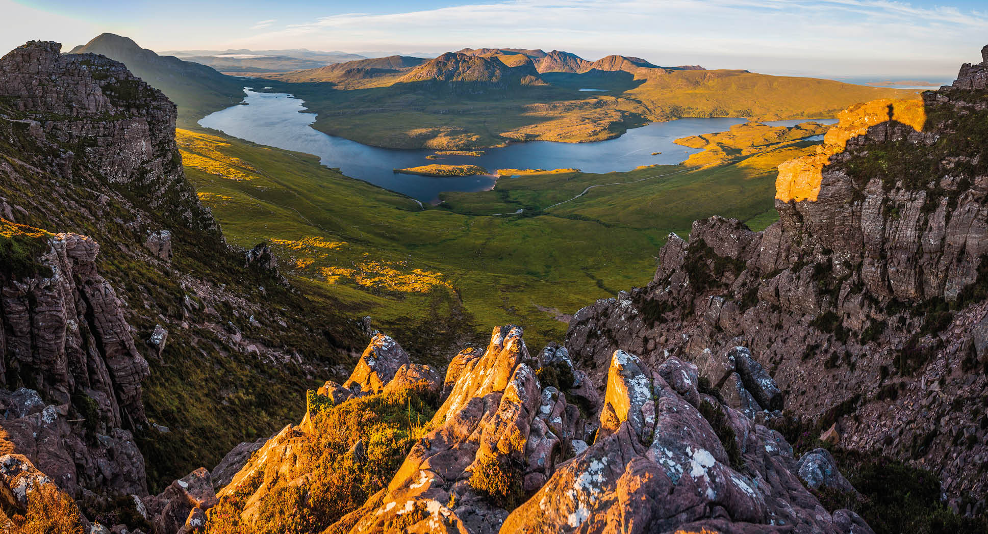 Golden sunrise illuminating the dramatic mountain peaks, glens and ridges of Coigach overlooking Loch Lugainn on the wild and remote peninsula deep in the Northwest Highlands of Scotland, UK.