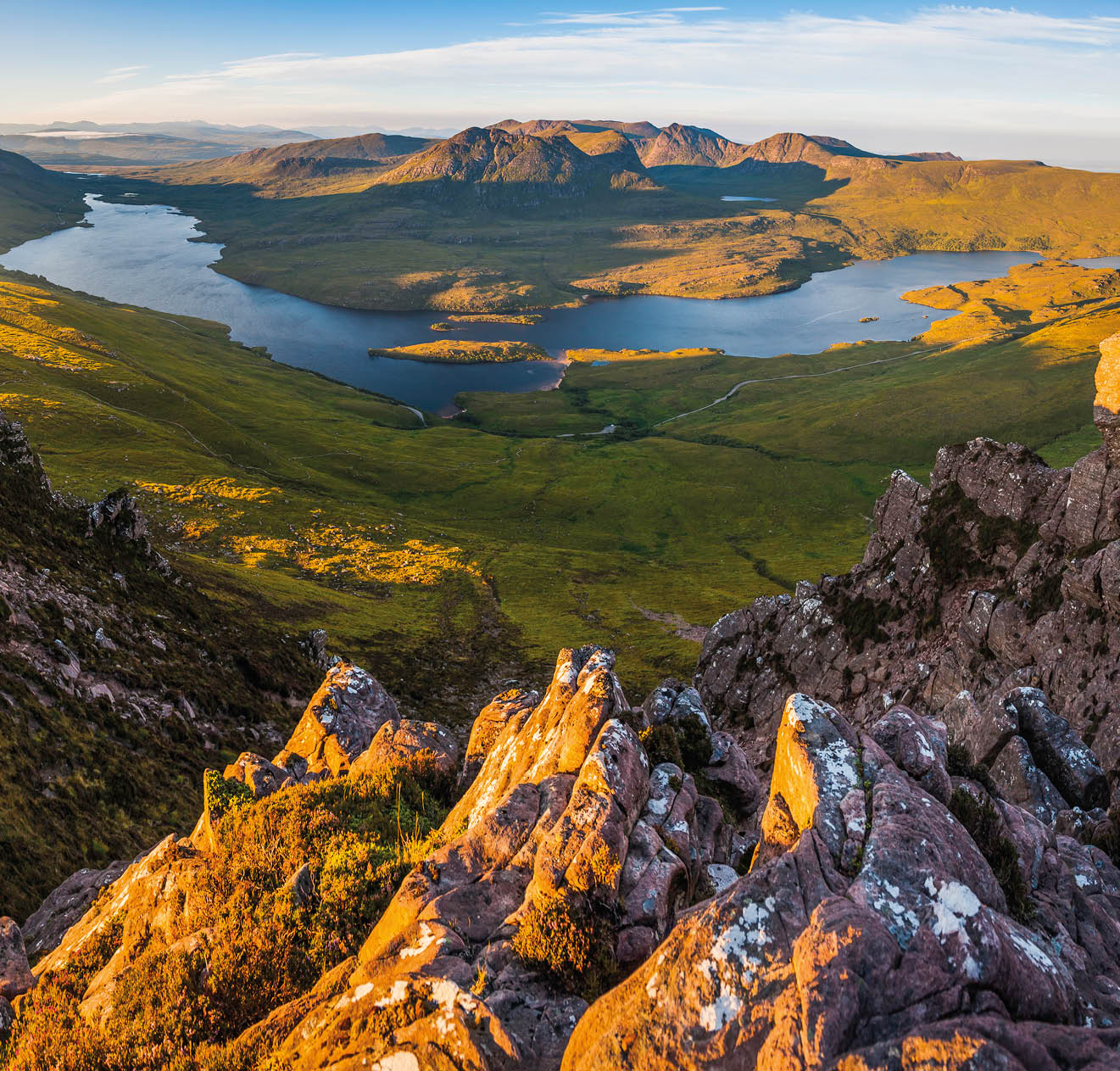 Golden sunrise illuminating the dramatic mountain peaks, glens and ridges of Coigach overlooking Loch Lugainn on the wild and remote peninsula deep in the Northwest Highlands of Scotland, UK.